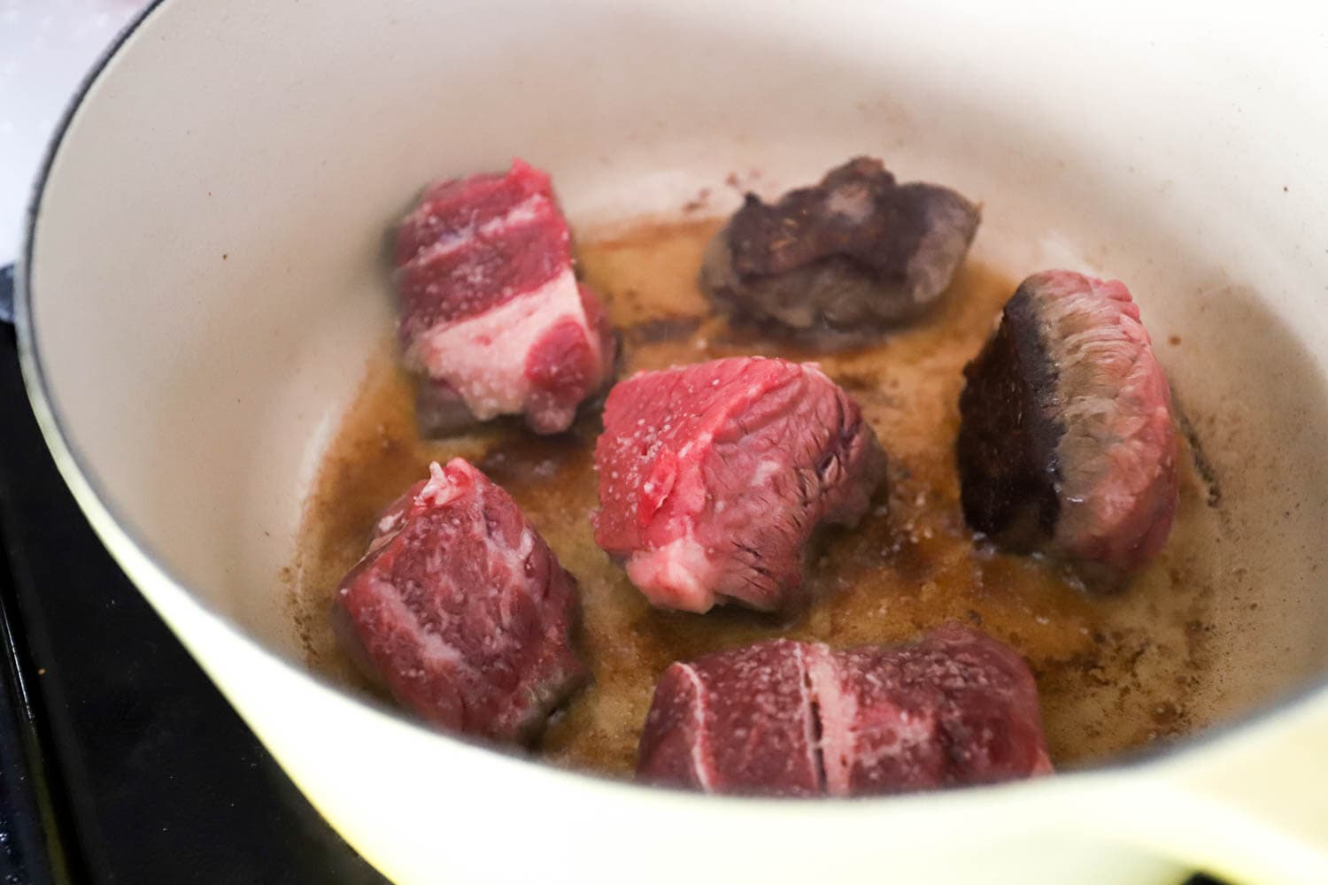 side view of pale yellow soup pot with partially browned beef chunks with brown bits on the bottom of the pot.