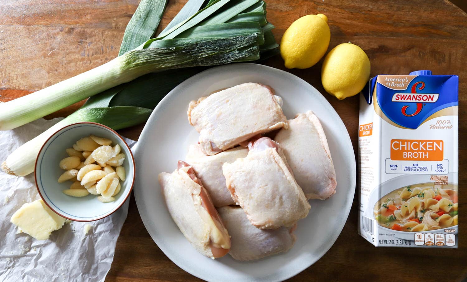 Ingredients for chicken and leeks sauce on a wooden cutting board.