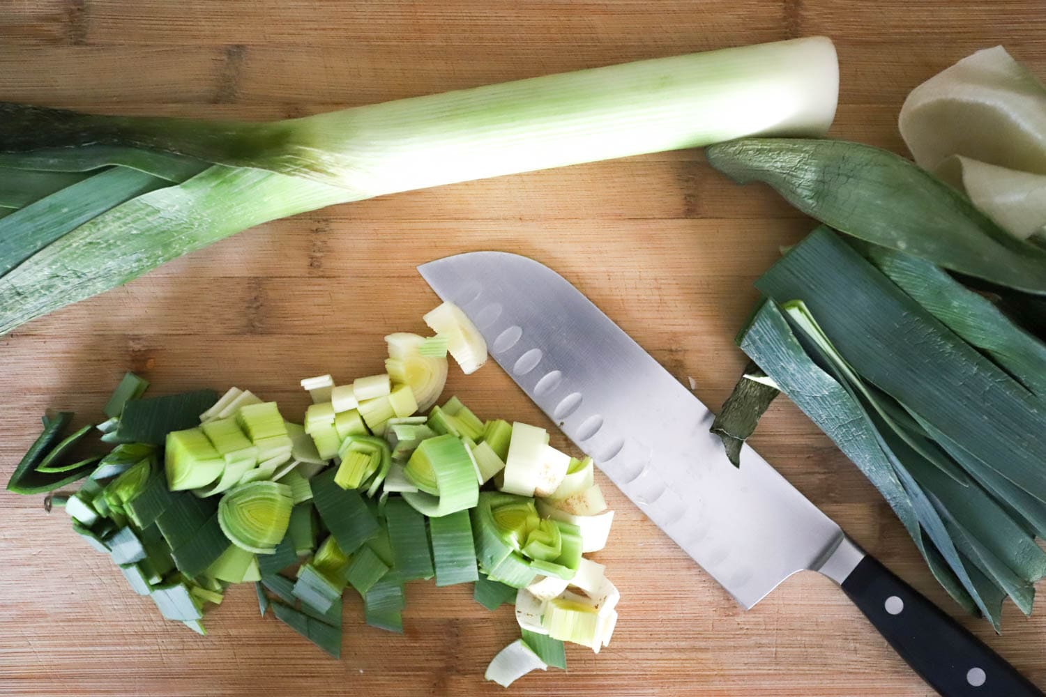 Sliced halved leeks on a cutting board with chef's knife.