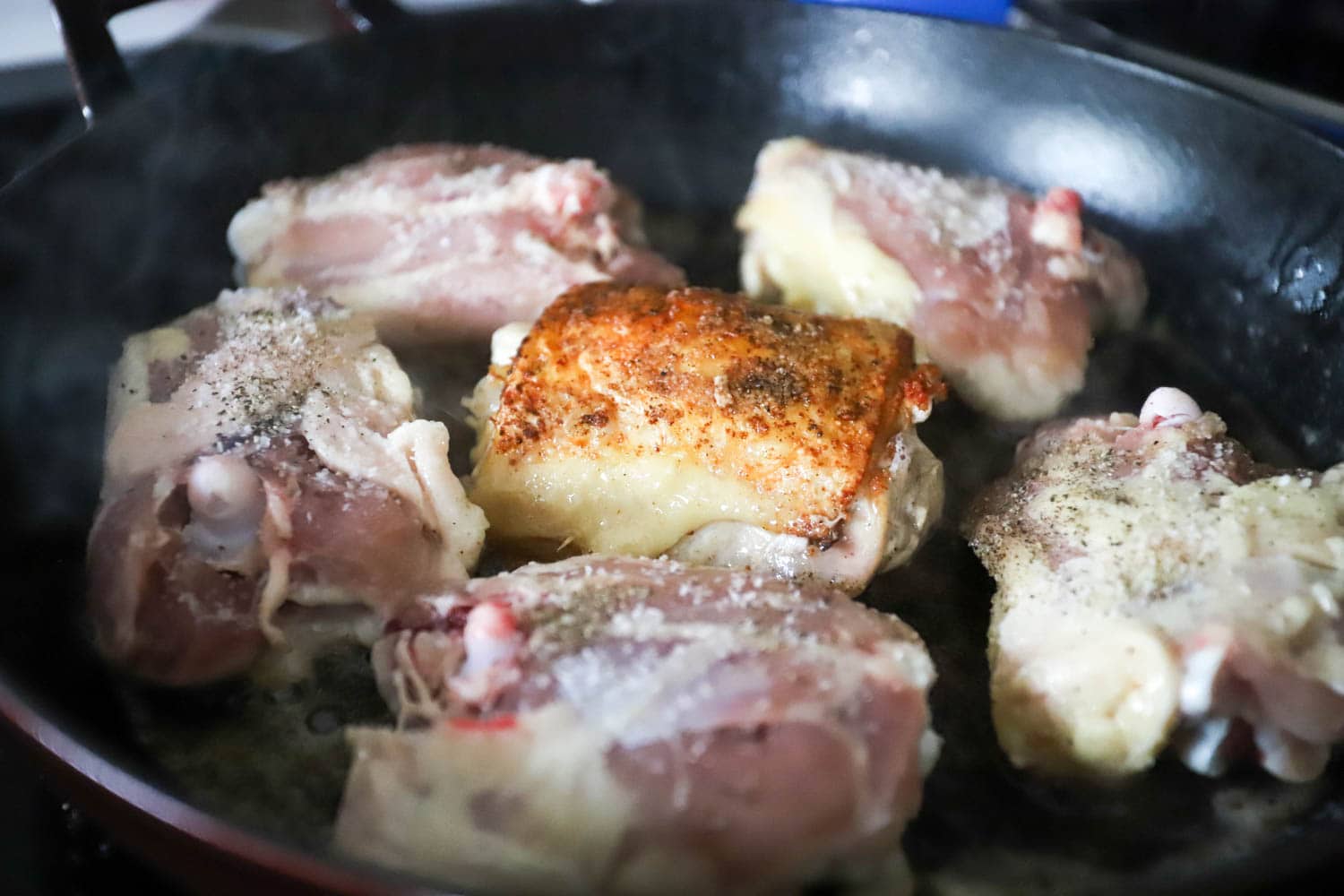 cast iron skillet with chicken thighs searing.