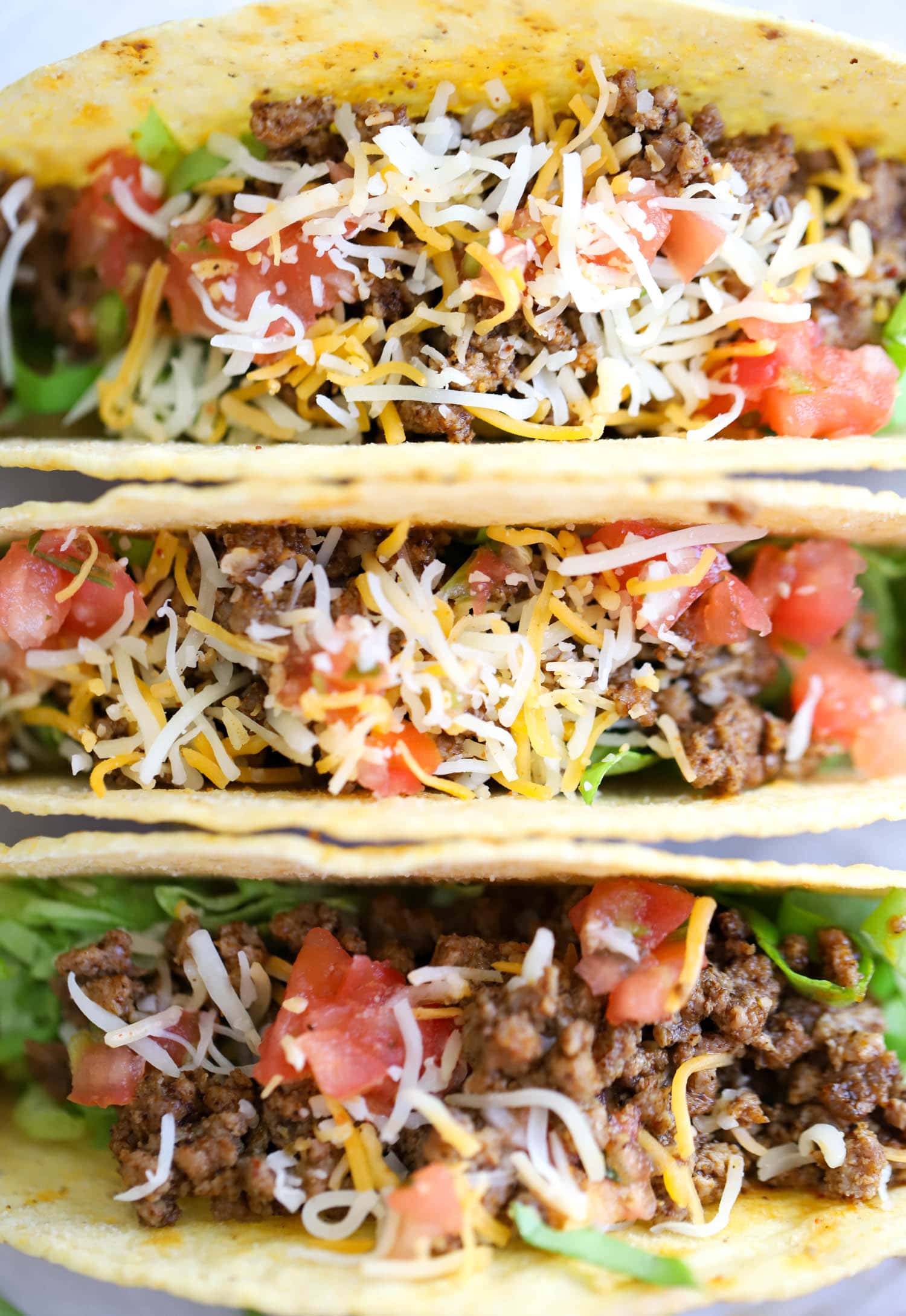 close up hard shell beef tacos topped with cheese.
