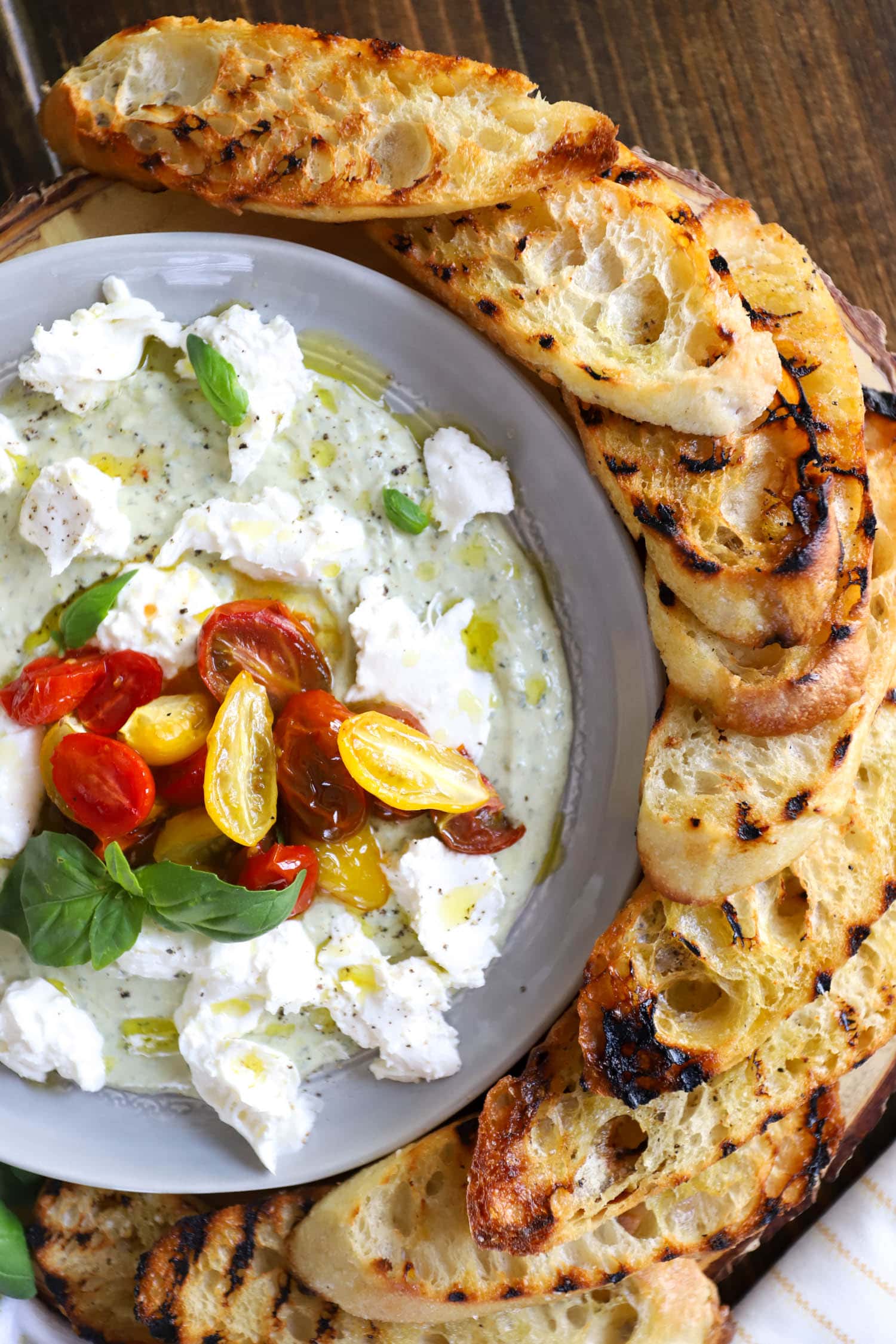 Gray plate with burrata, pesto, and roasted tomatoes surrounded by grilled bread.