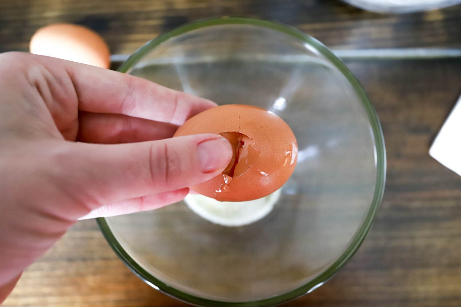 Hand holding a cracked egg over a batter bowl.