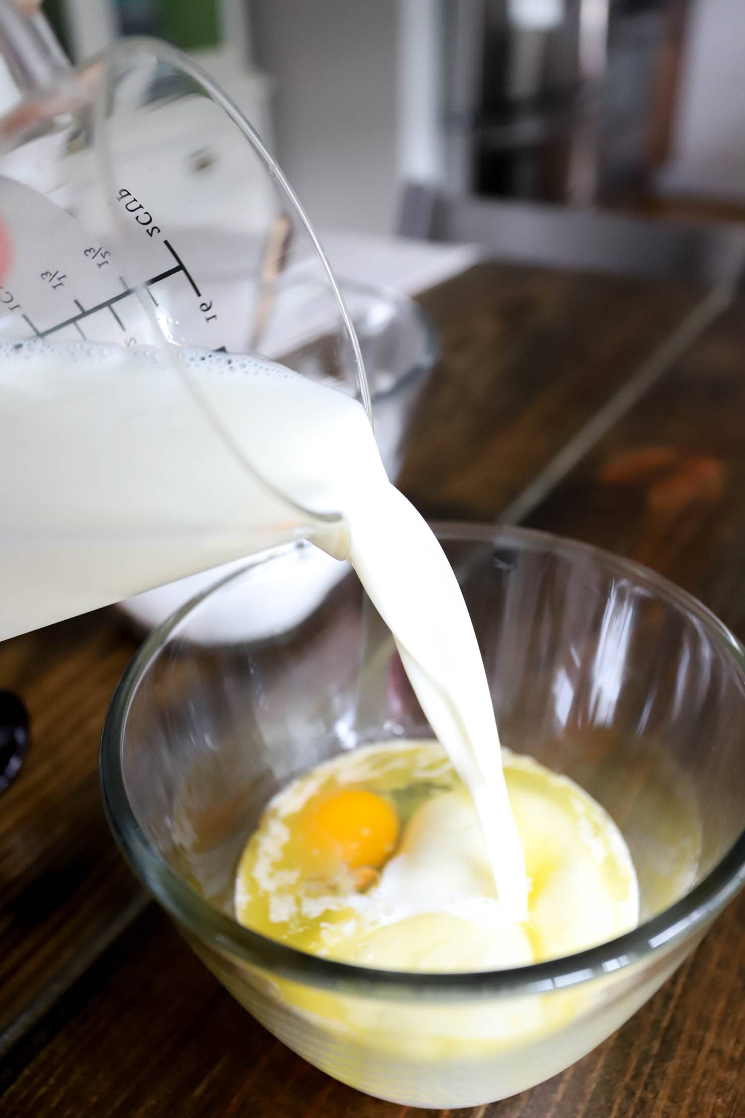 Glass measuring cup pouring milk into a large mixing bowl.