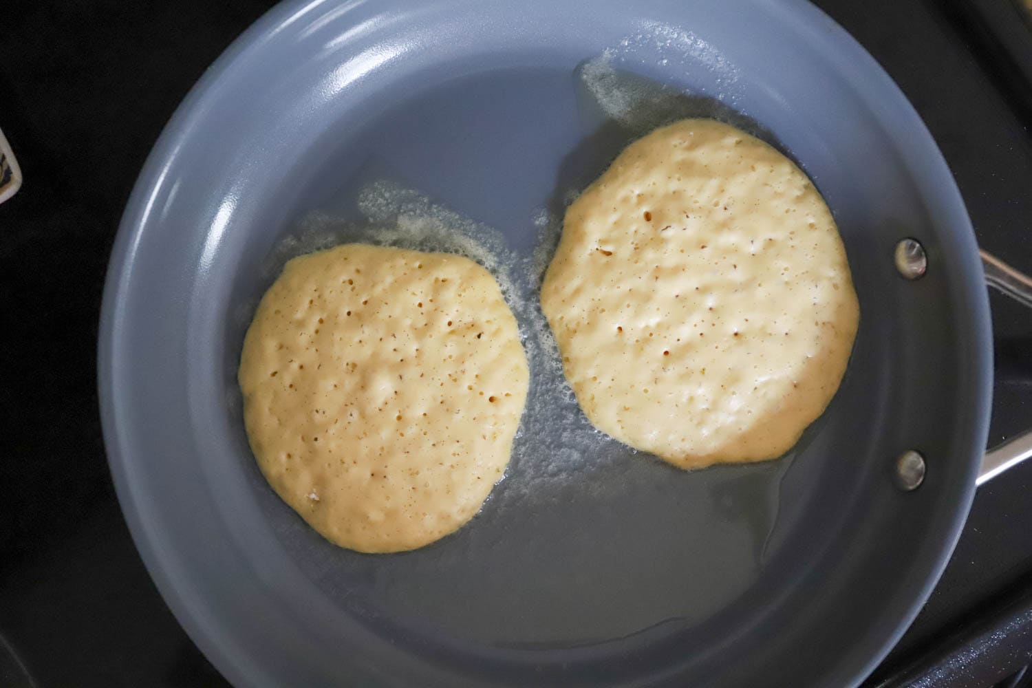 Two pancakes cooking in butter on a nonstick blue pan.