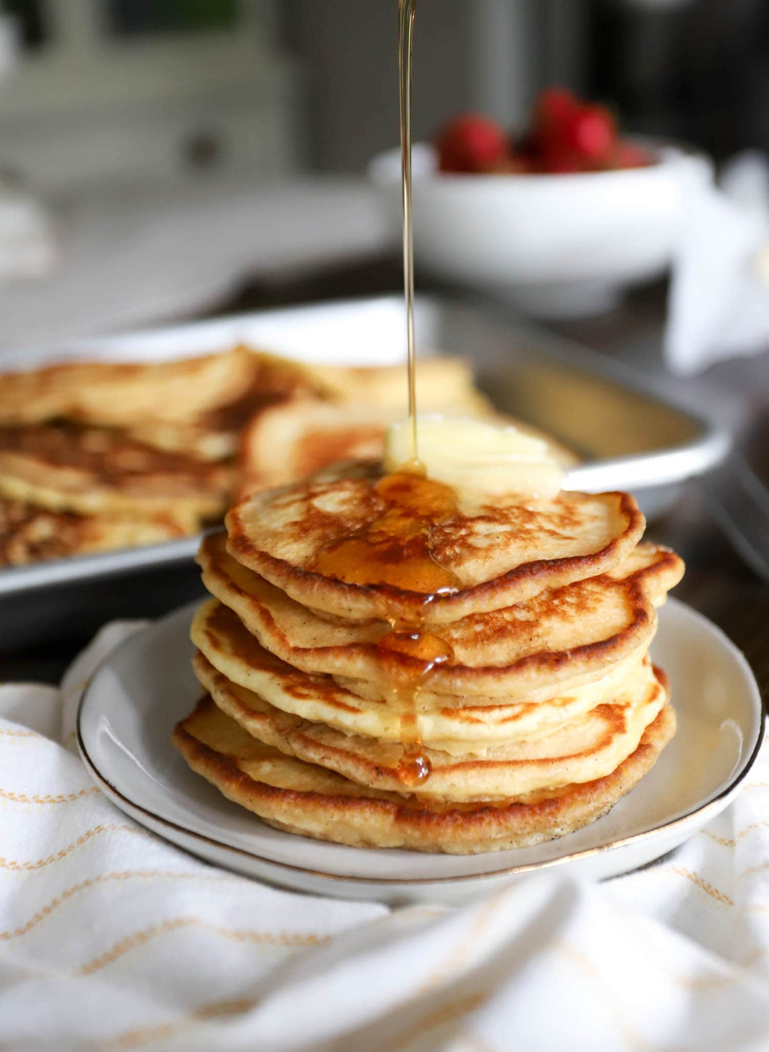 Tall stack of pancakes with stream of syrup being poured over top.