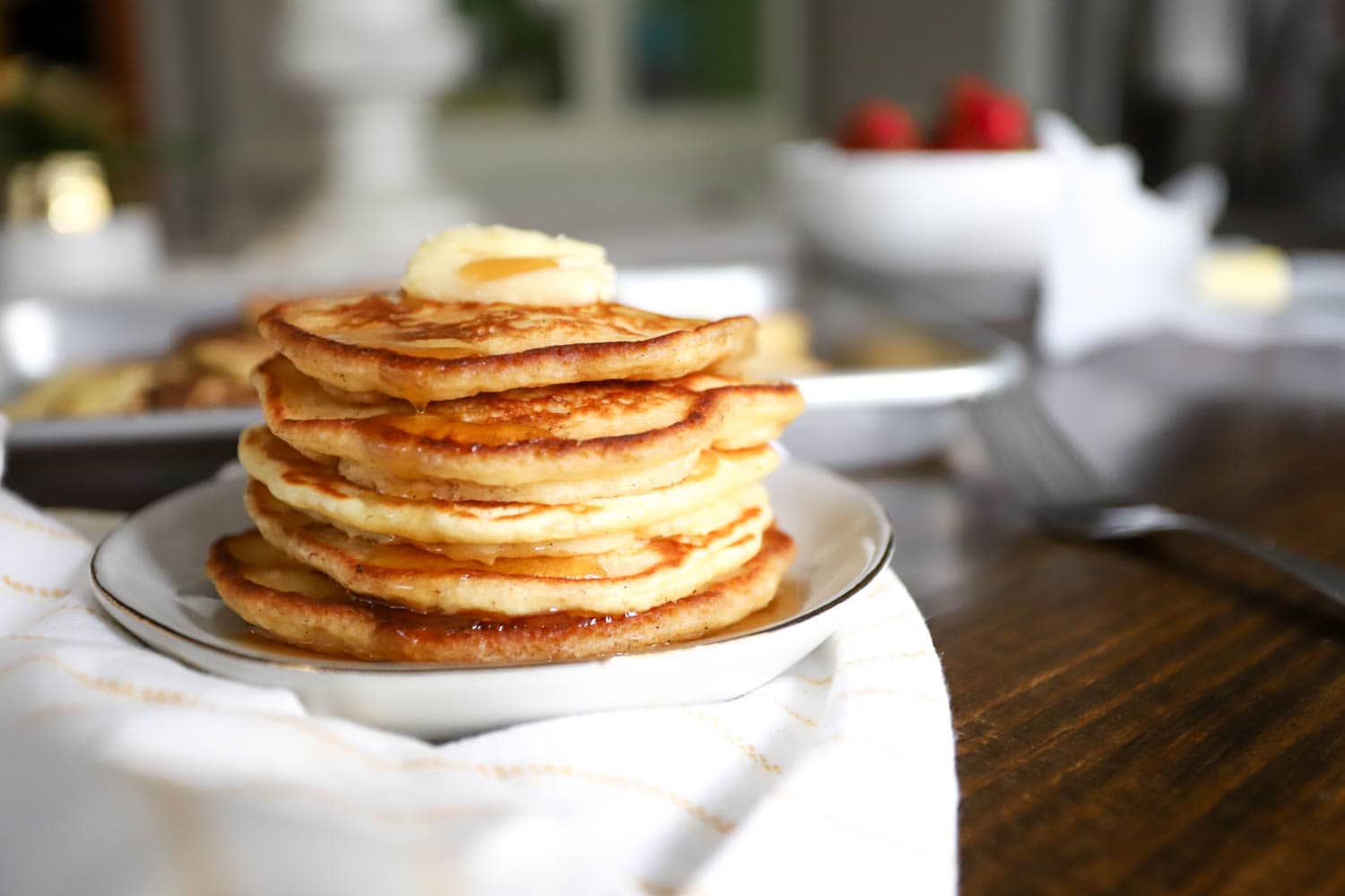 Stack of basic pancakes topped with syrup and butter on small white ceramic plate.