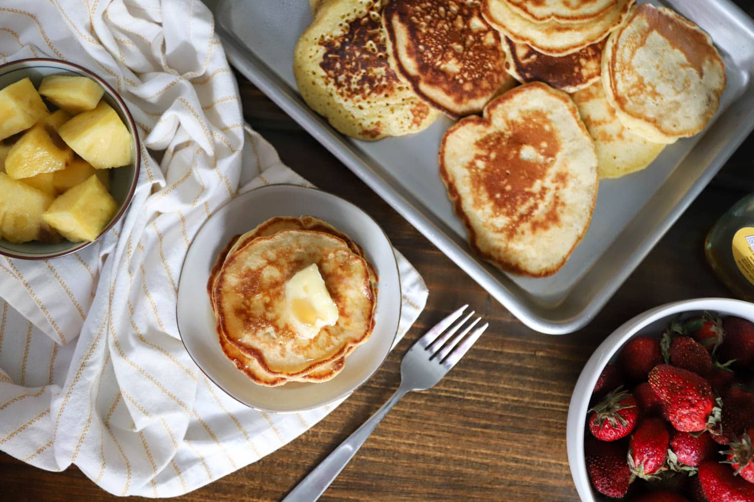 Top view of nyt pancakes on a large serving tray surrounded by fruit and syrup.