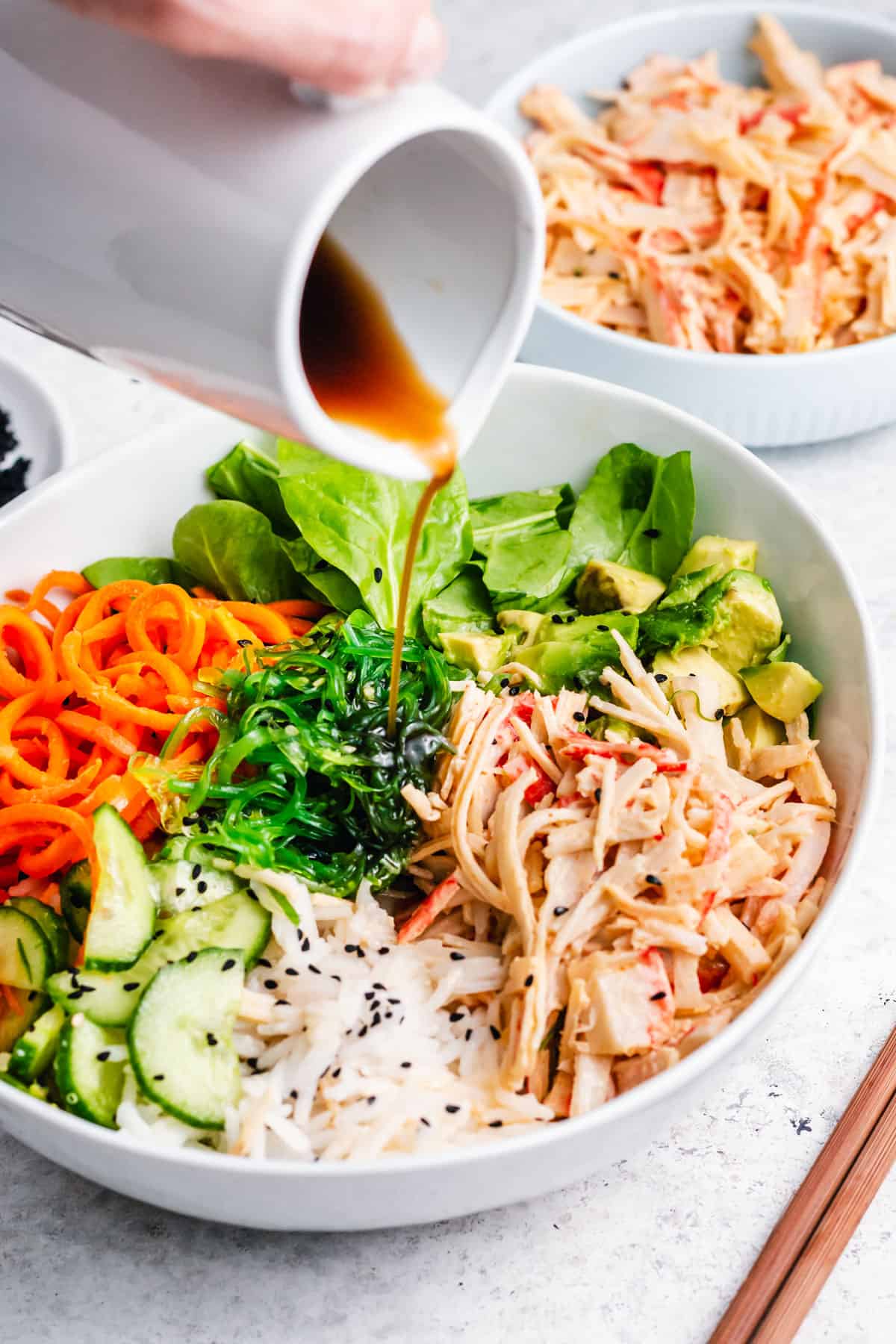 small pitcher pouring sweet soy over crab salad rice bowl.