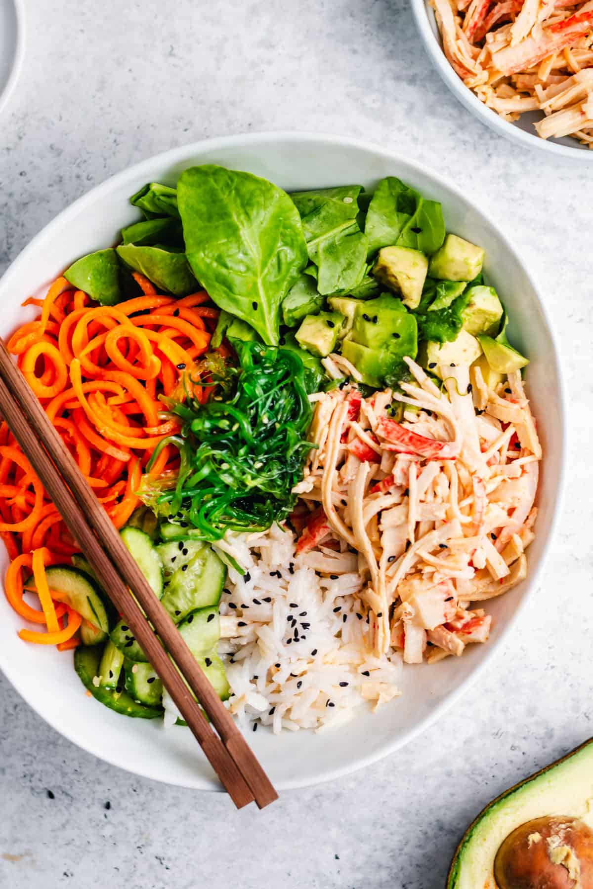 spicy crab salad poke bowl with carrots and spinach leaves on top.