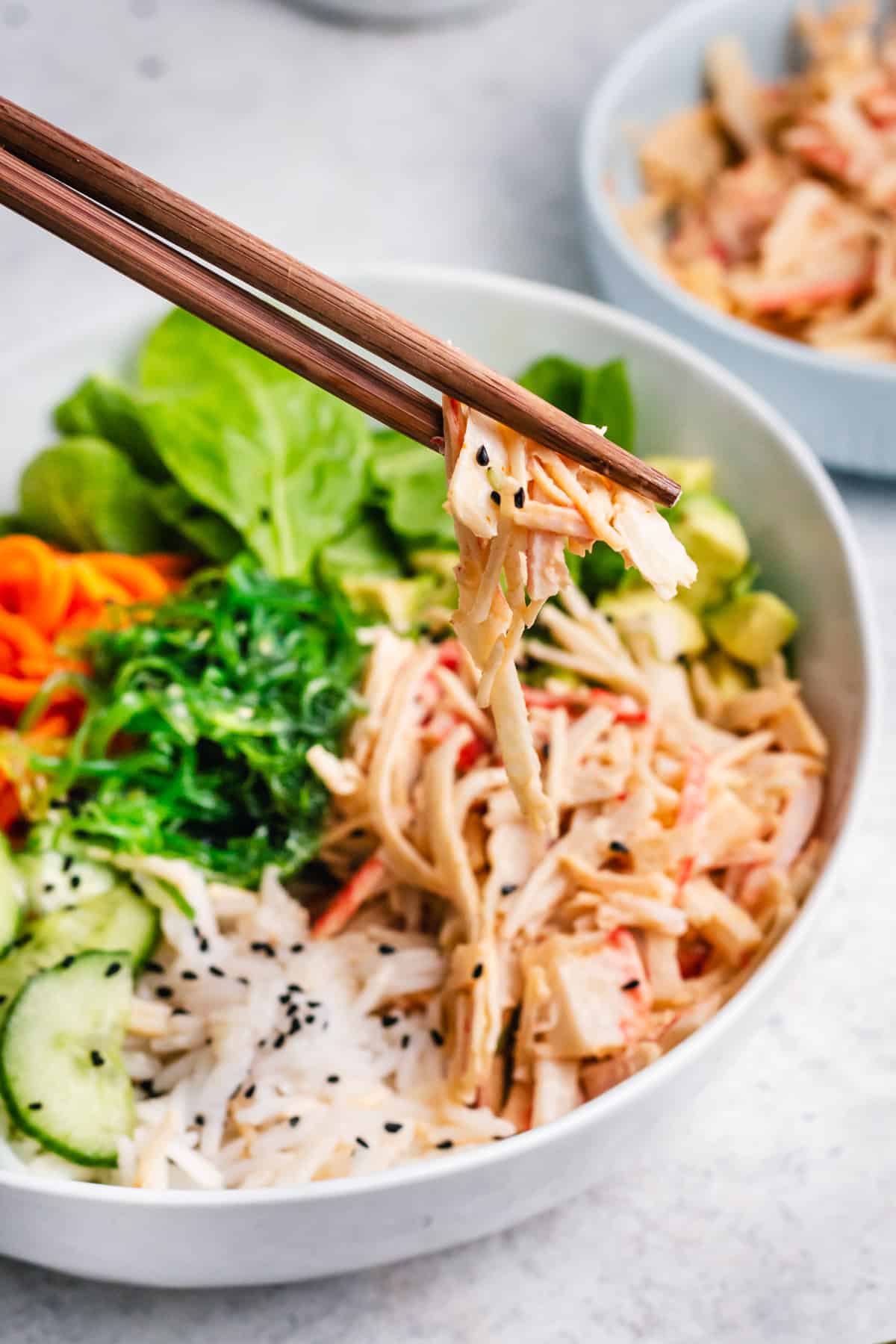 chopsticks with bite of spicy crab salad in rice bowl.