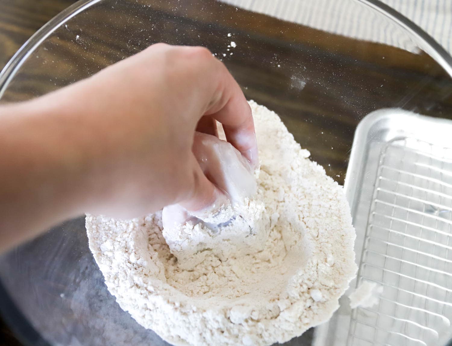 hand dredging chicken pieces in flour