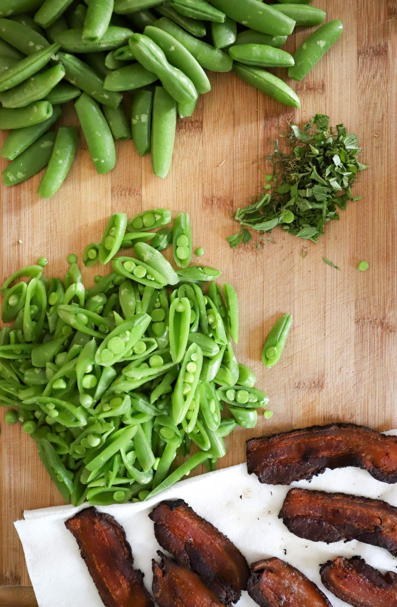 wood board with sliced sugar snap peas and bacon.