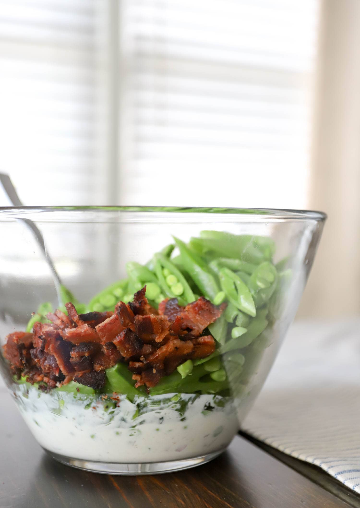 side view glass bowl with bacon and snap peas.