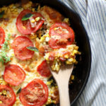 skillet of tomatoes and corn with wooden spoon