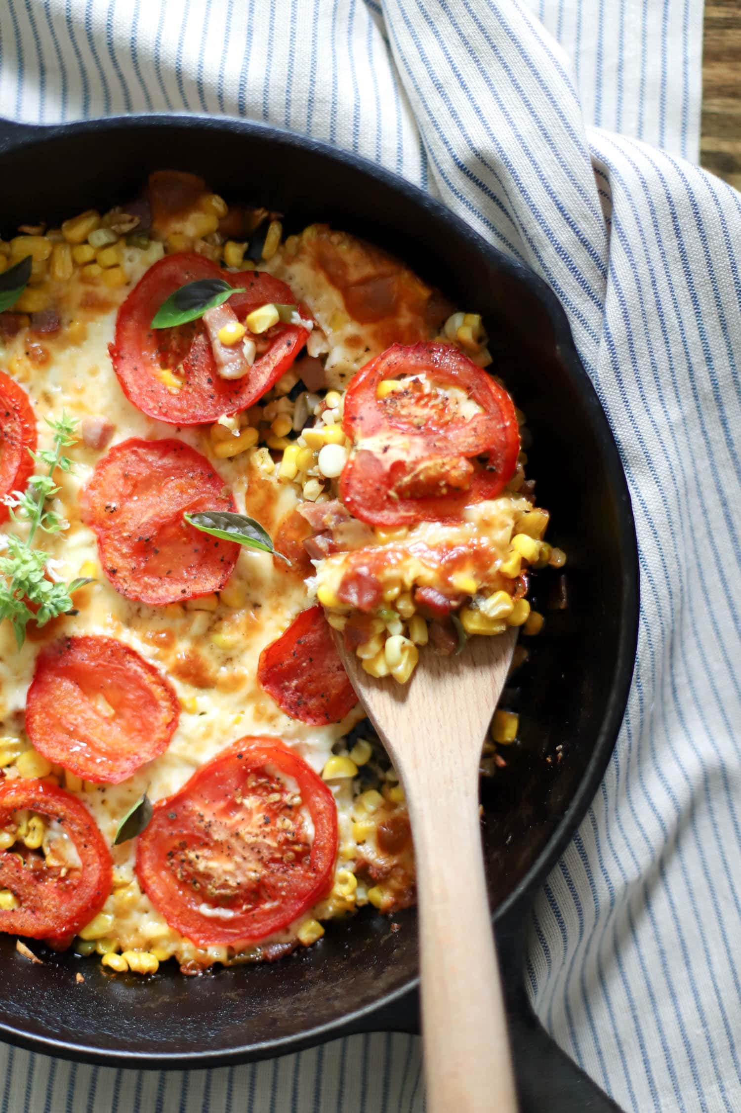 skillet of tomatoes and corn with wooden spoon