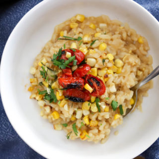corn risotto bowl topped with green onions and blistered cherry tomatoes