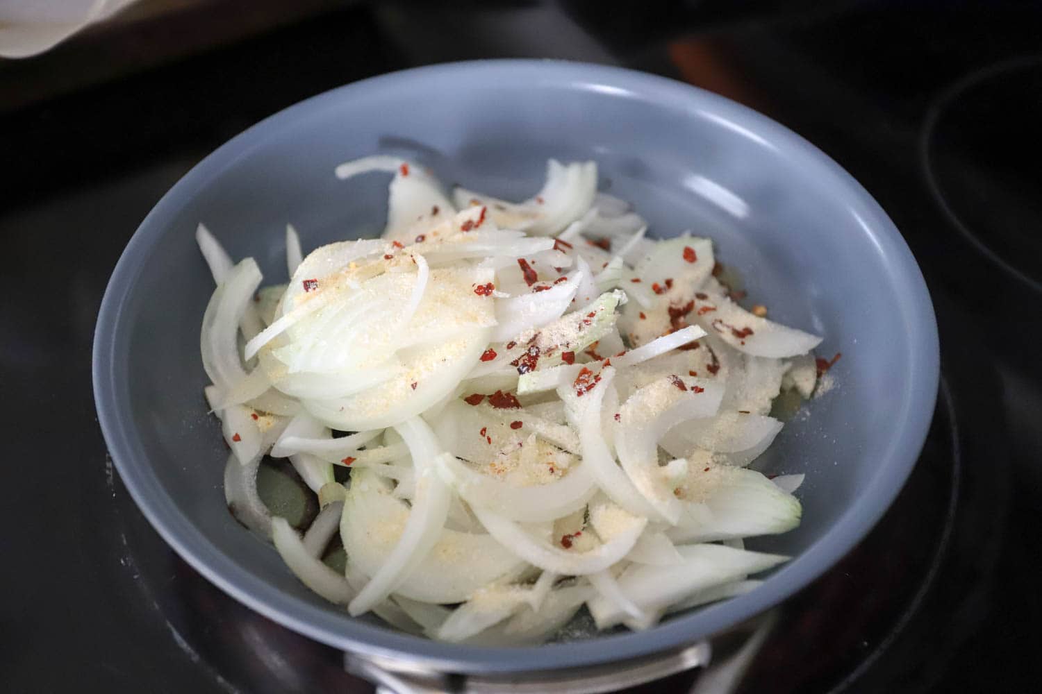 Blue nonstick skillet with raw onions and spices.