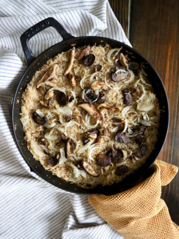 Black skillet with stick of butter rice with mushrooms.