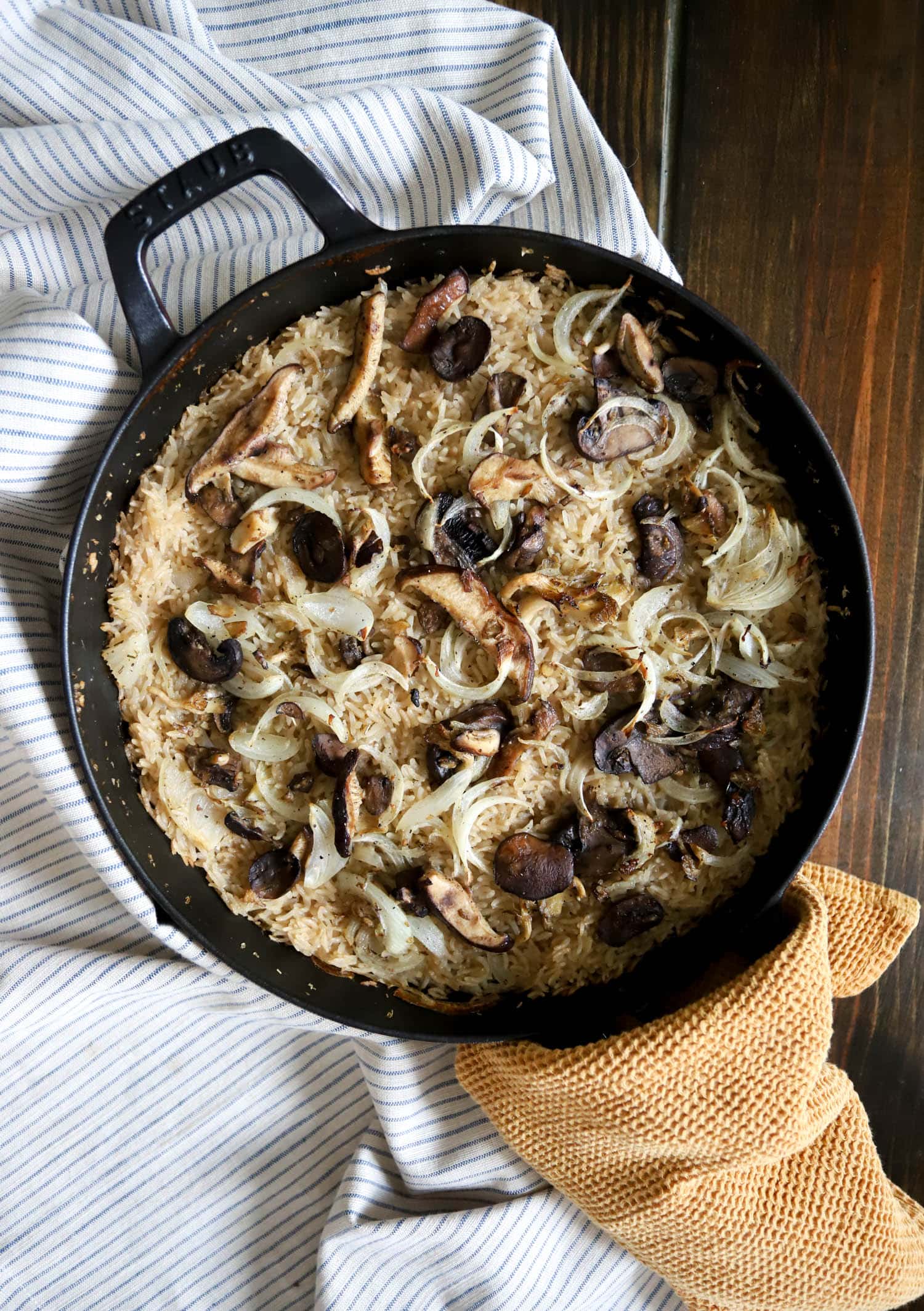 top view of a black pan with baked rice topped with mushrooms and onions.