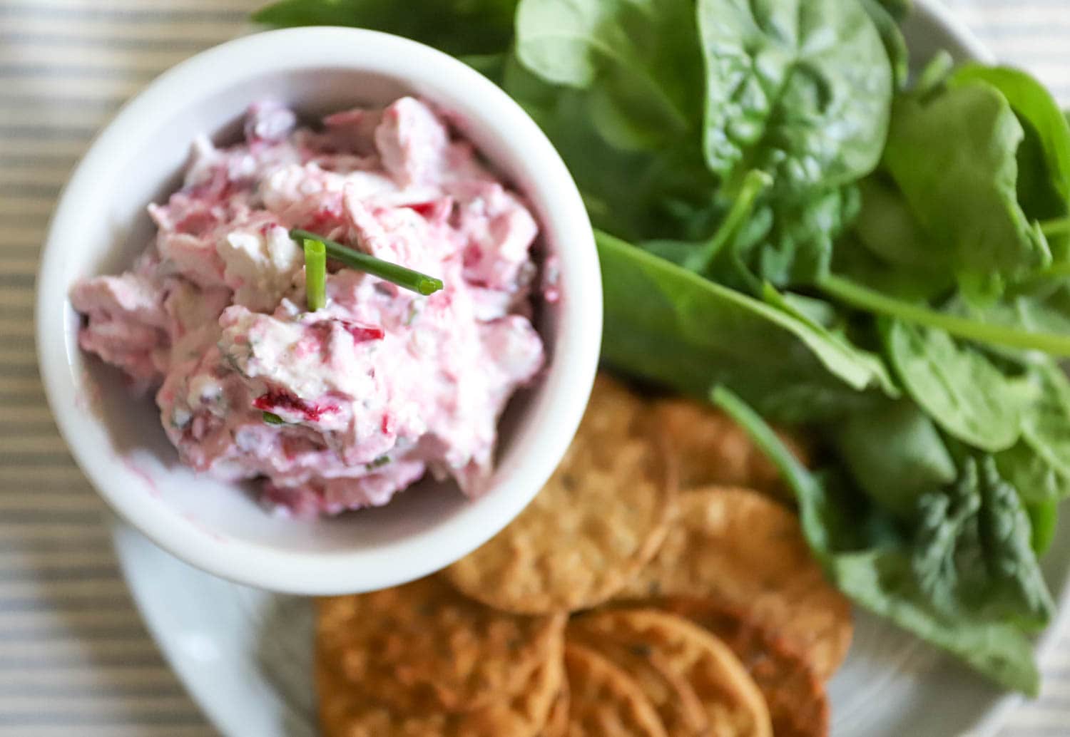 small white bowl with cranberry turkey salad on a plate with crackers and spinach.