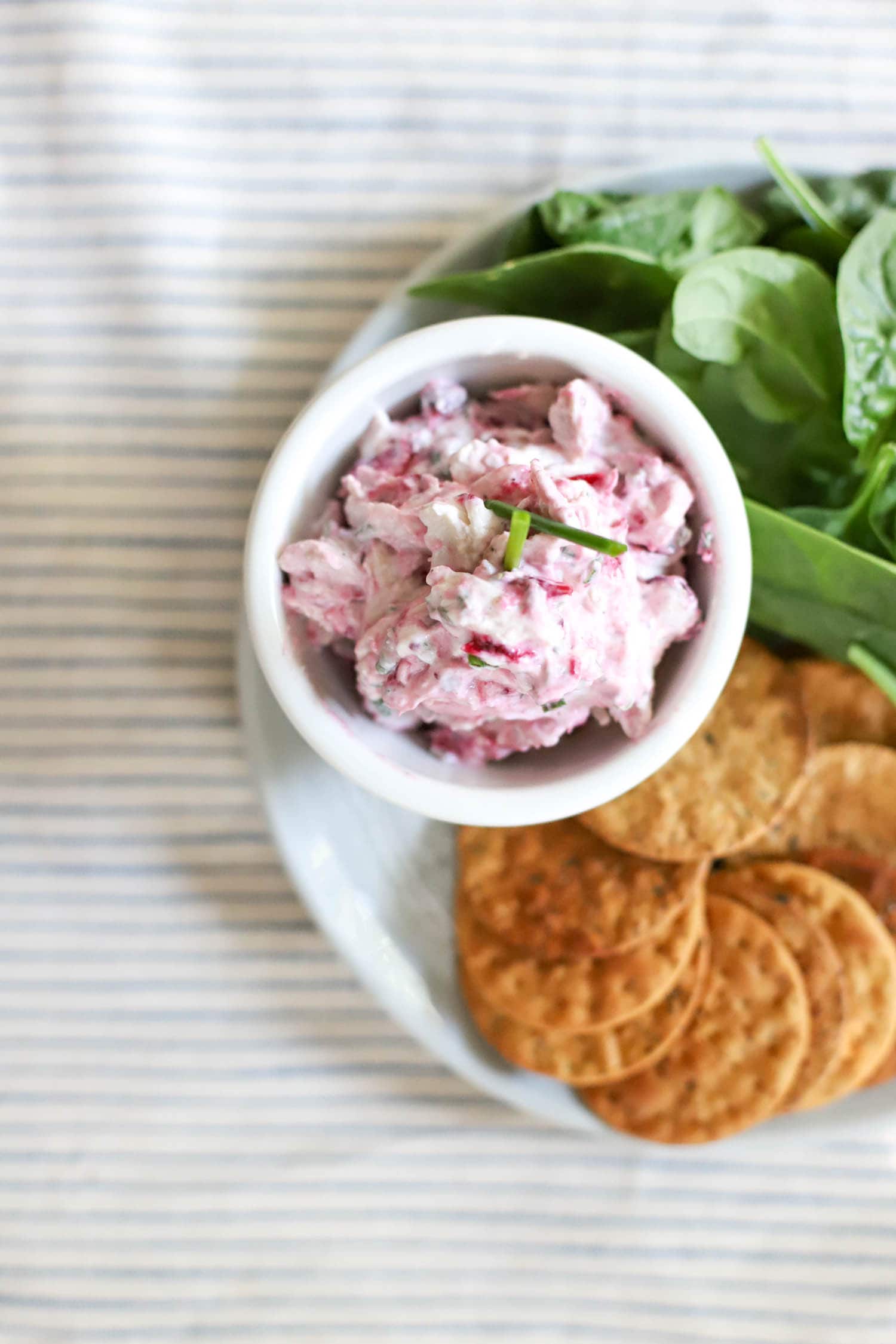 bowl of pink cranberry turkey salad on striped napkin with spinach leaves on the side.