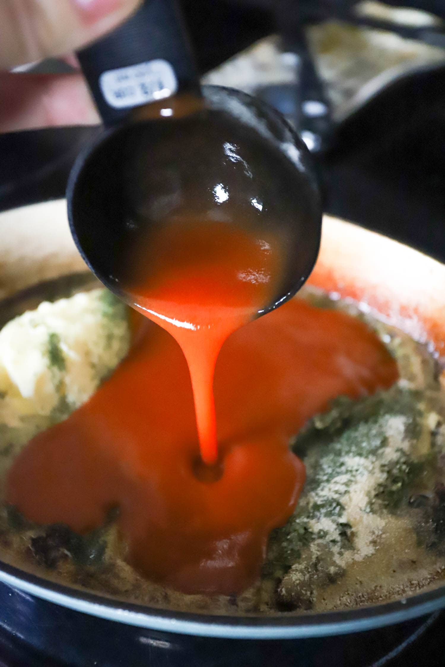 hand pouring hot sauce into a skillet with seasonings.