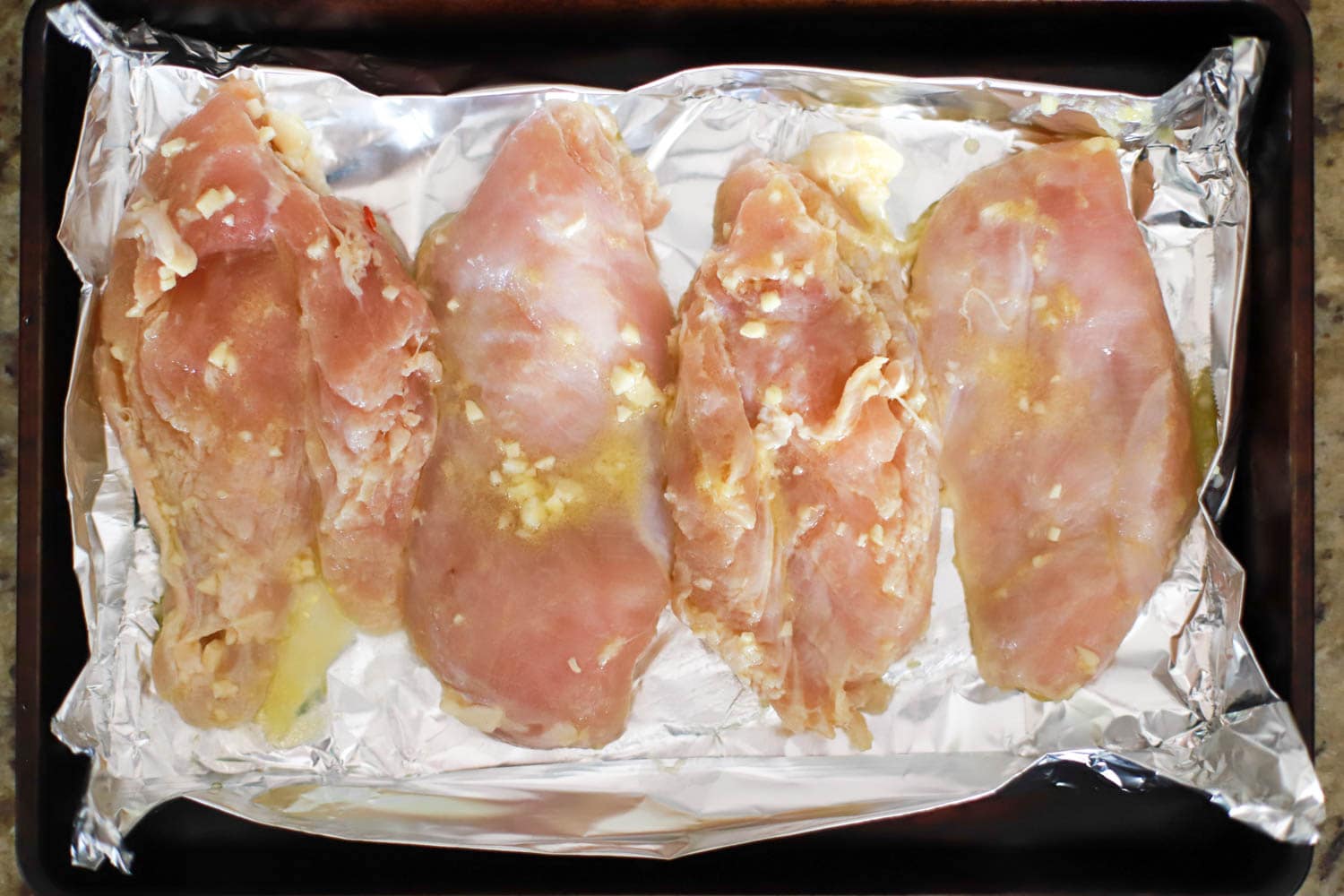 raw chicken breasts with garlic lemon marinade on sheet pan with aluminum foil