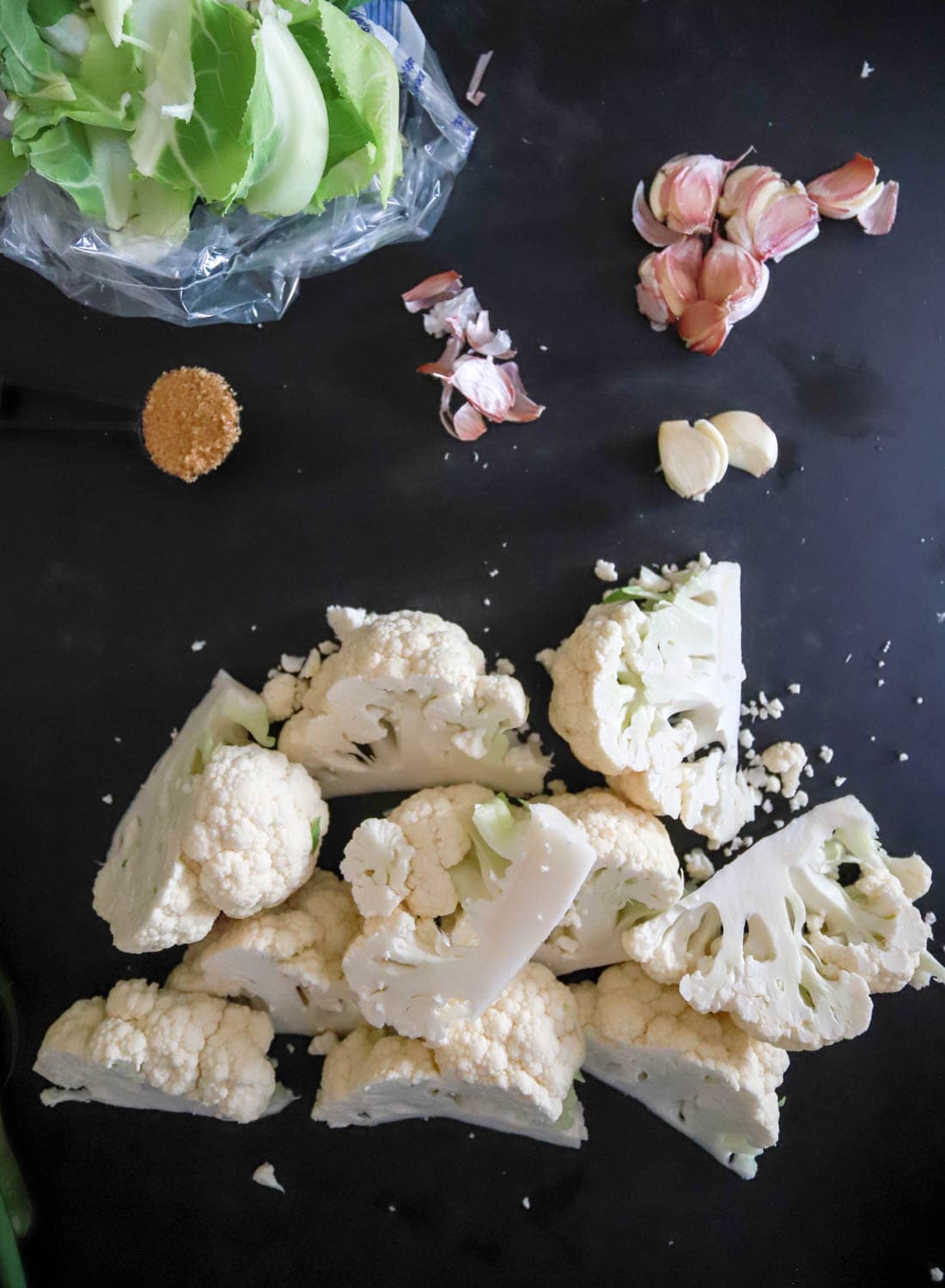 cut up cauliflower wedges with smashed garlic cloves on black cutting board.