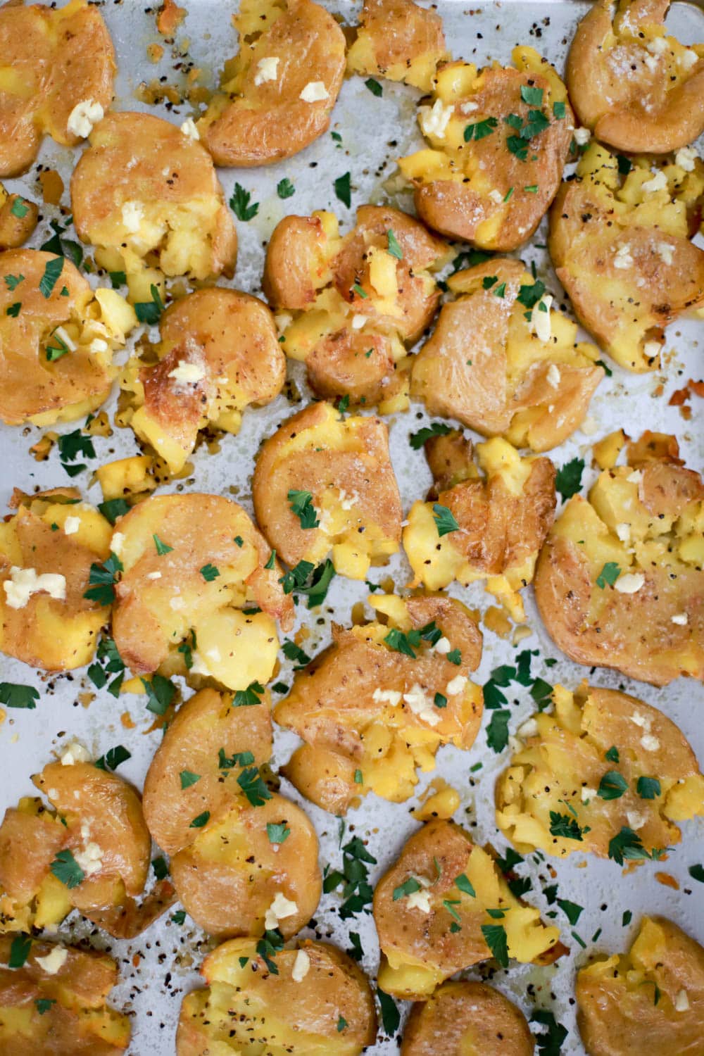 sheet pan of crispy smashed potatoes covered in garlic and sprinkled with fresh parsley.