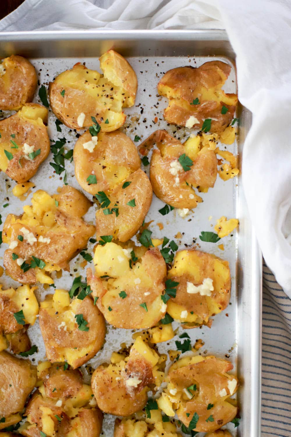 Sheet pan of crispy smashed potatoes close up with white napkin on the edge.