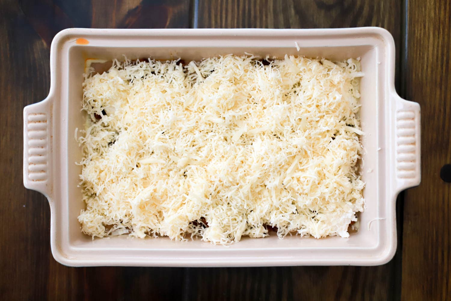 rectangular baking dish with unbaked refried bean dip topped with cheese.