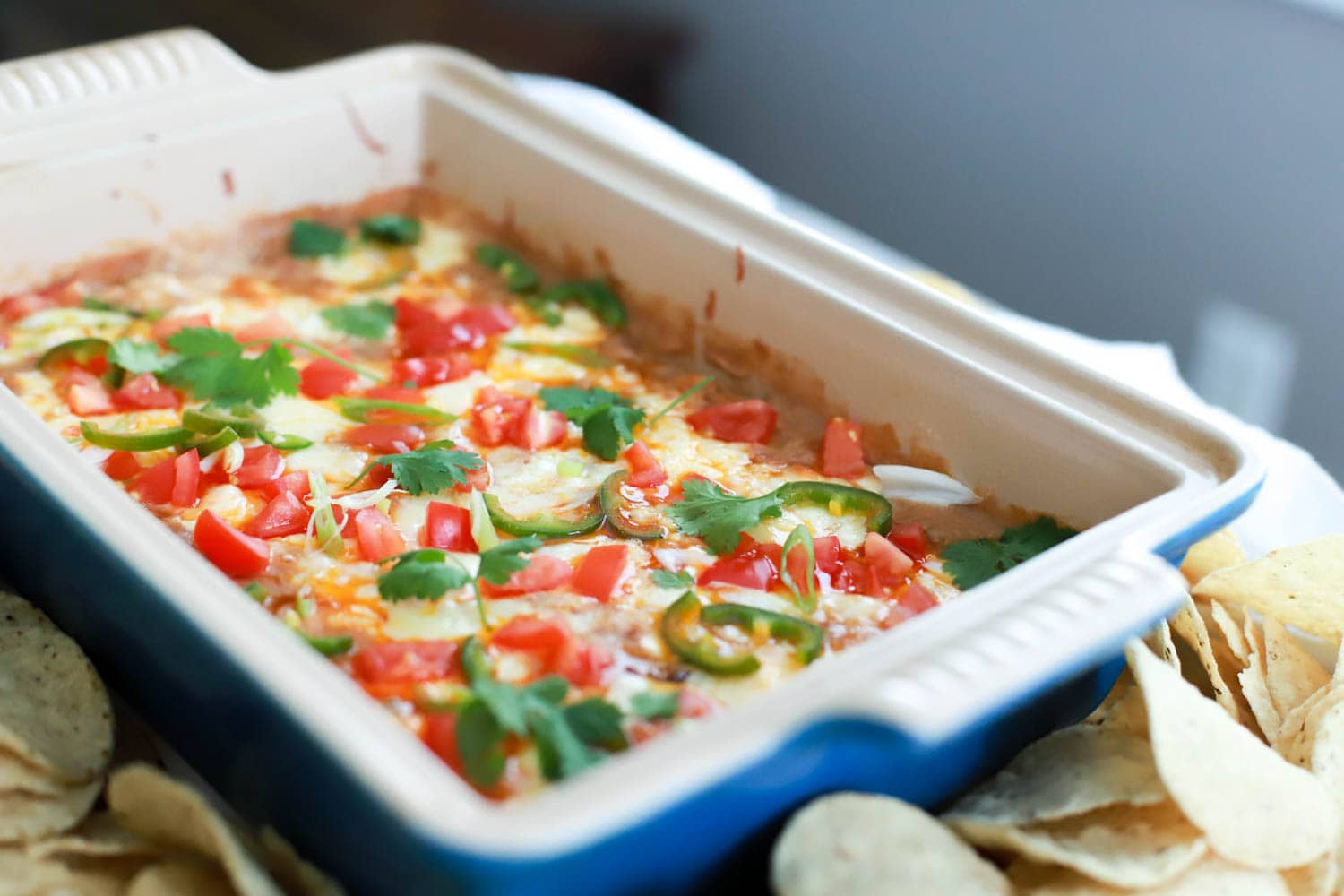Blue baking dish of hot bean dip topped with cilantro and tomatoes.