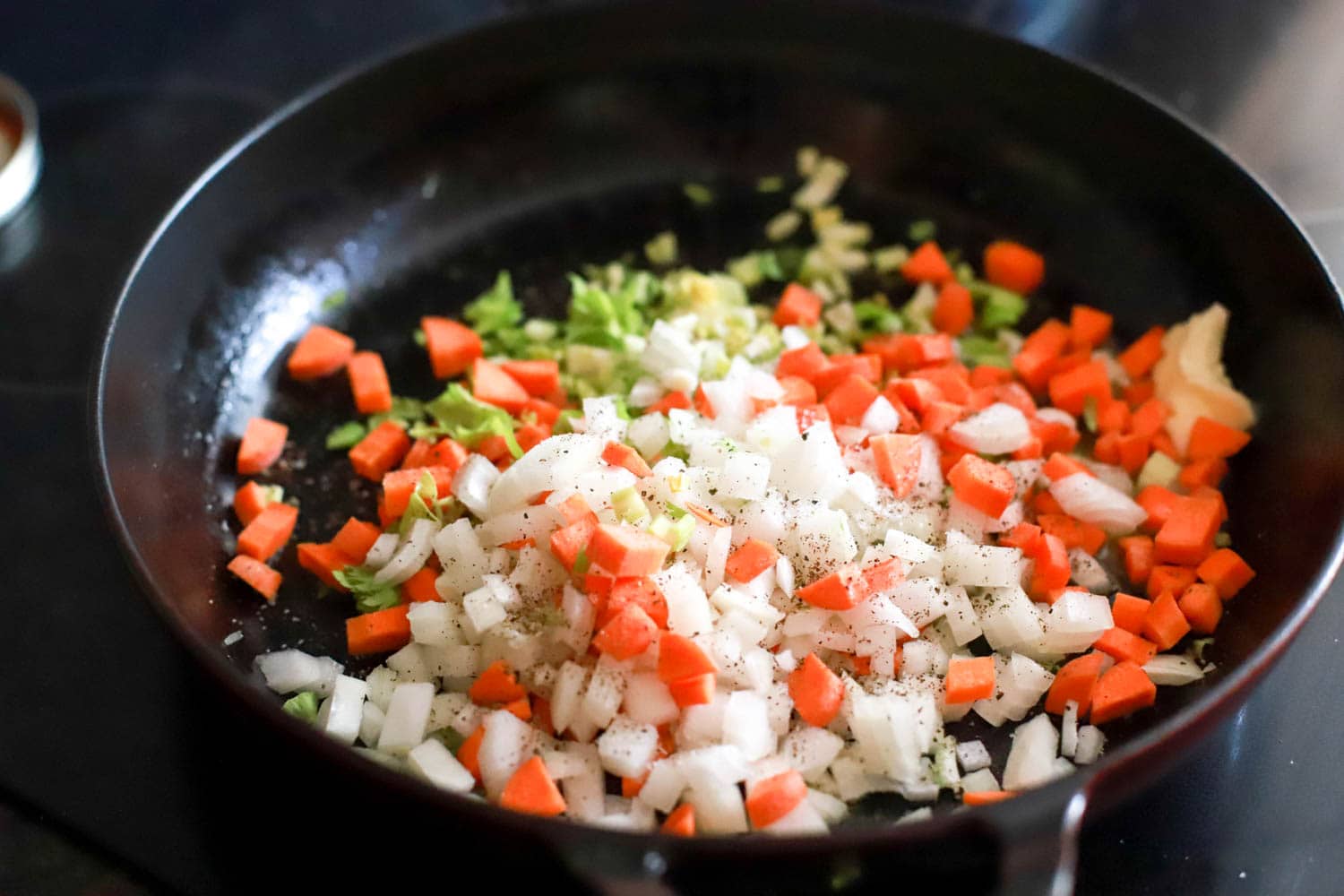 chopped raw vegetable base with salt and pepper in black skillet.