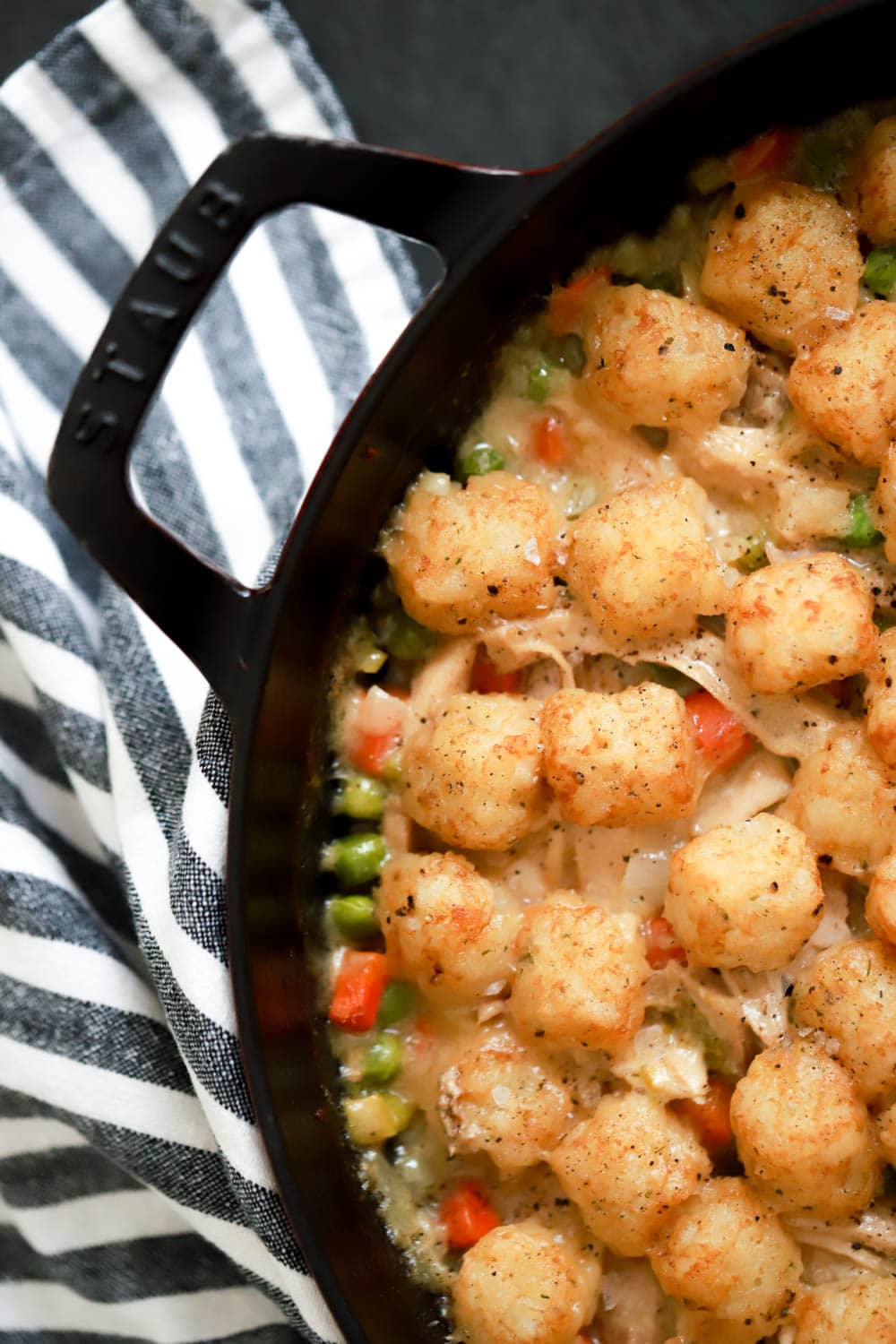 close up portion of skillet with chicken pot pie filling and tater tots on top.