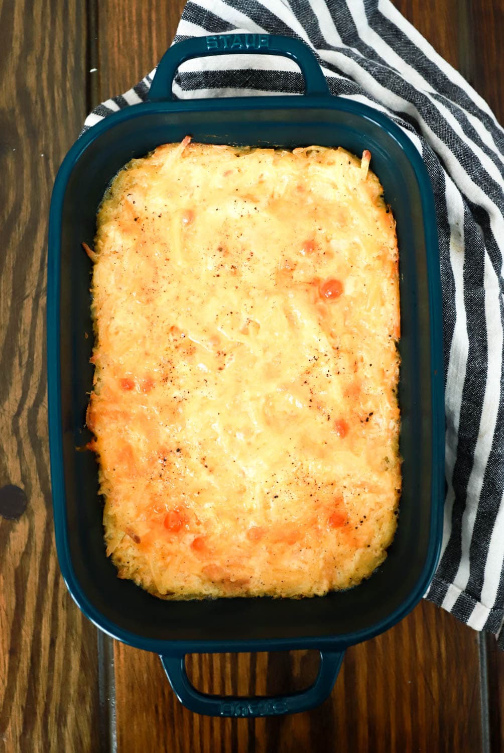 baked hash brown casserole in dark green baking dish top view on brown table.