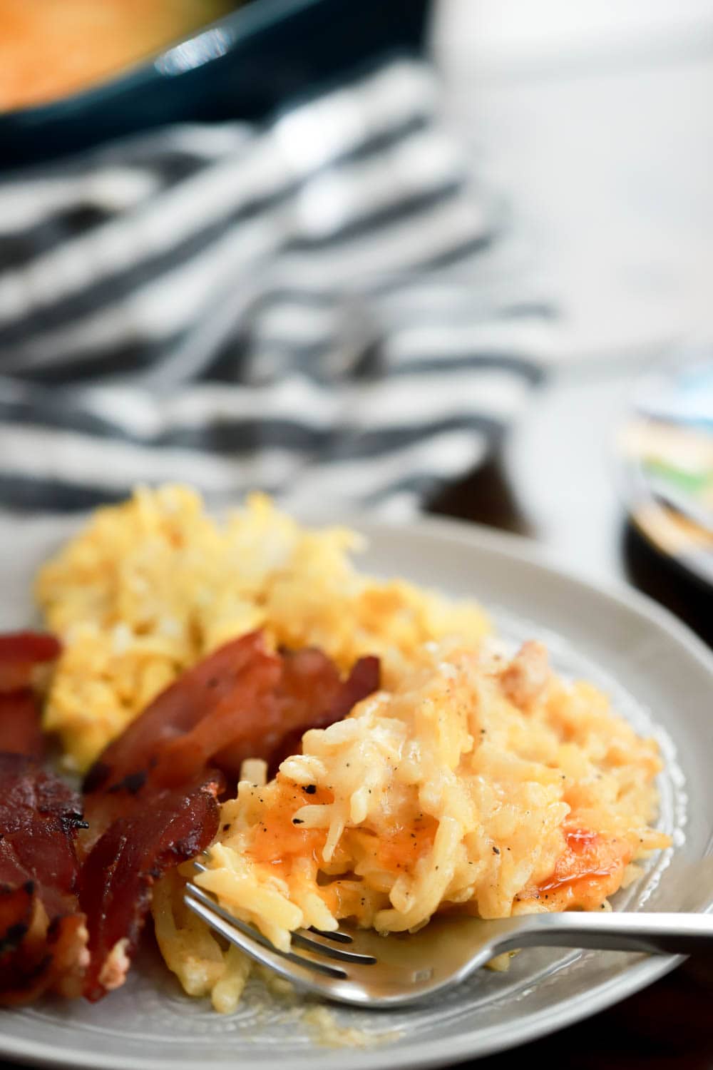 close up view of creamy hash brown casserole with bacon on the side.