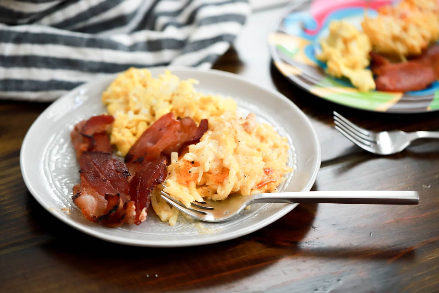Plate with small fork, bacon, eggs, and hashbrown casserole on table.