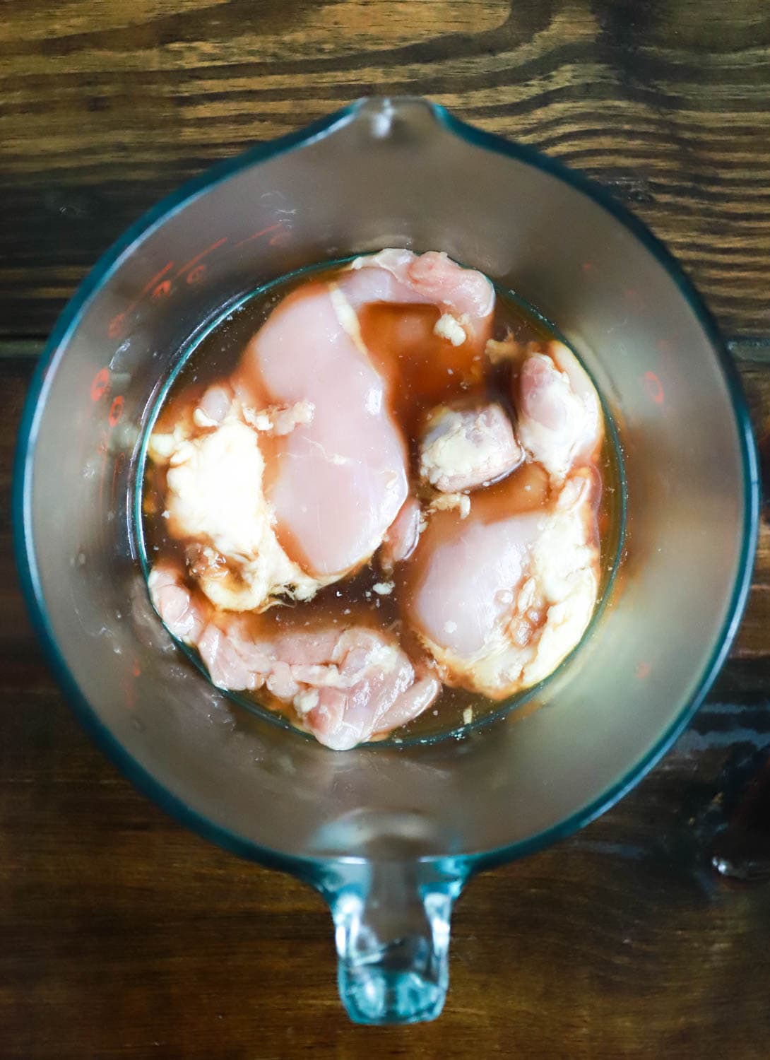 Glass bowl of raw chicken in marinade.