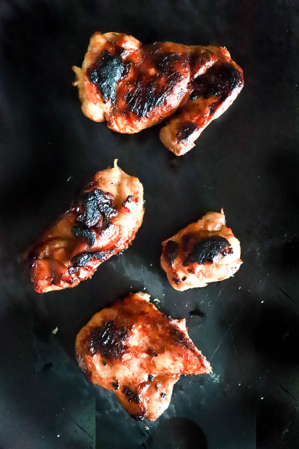 Grilled charred chicken thighs on a black cutting board.