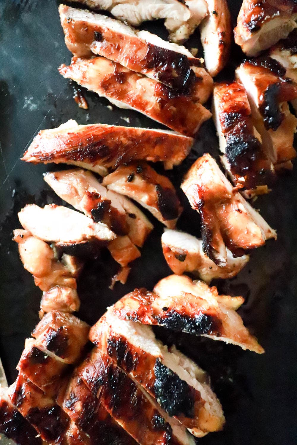 Sliced grilled chicken thighs on a black cutting board.