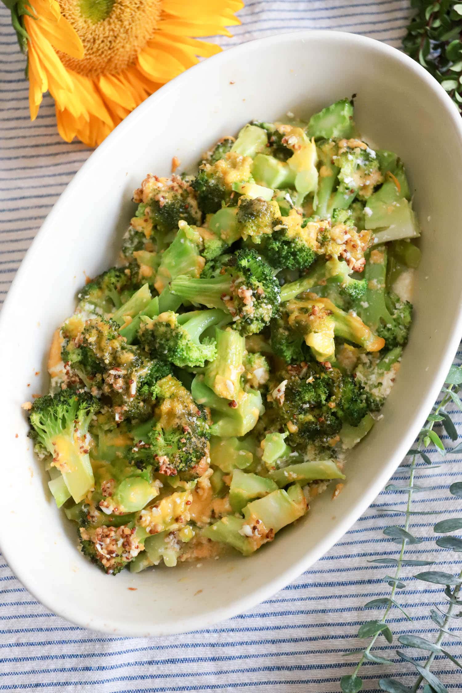 cheesy baked broccoli in a white baking dish with sunflower in the background.