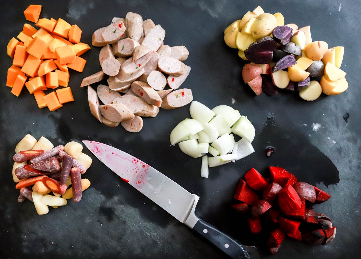 sheet pan dinner ingredients cut up on black board.