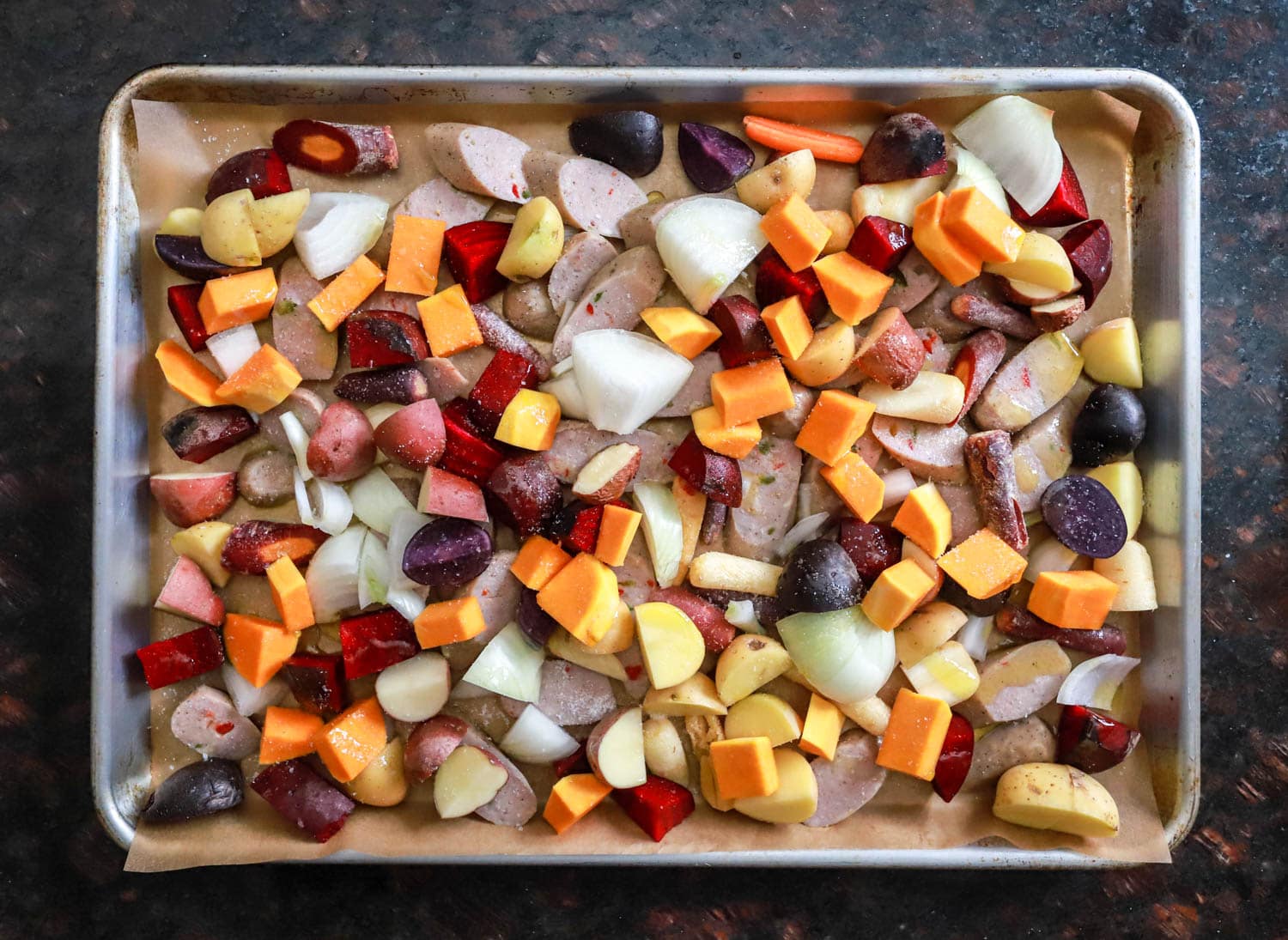 sheet pan veggies and sausage uncooked on pan.