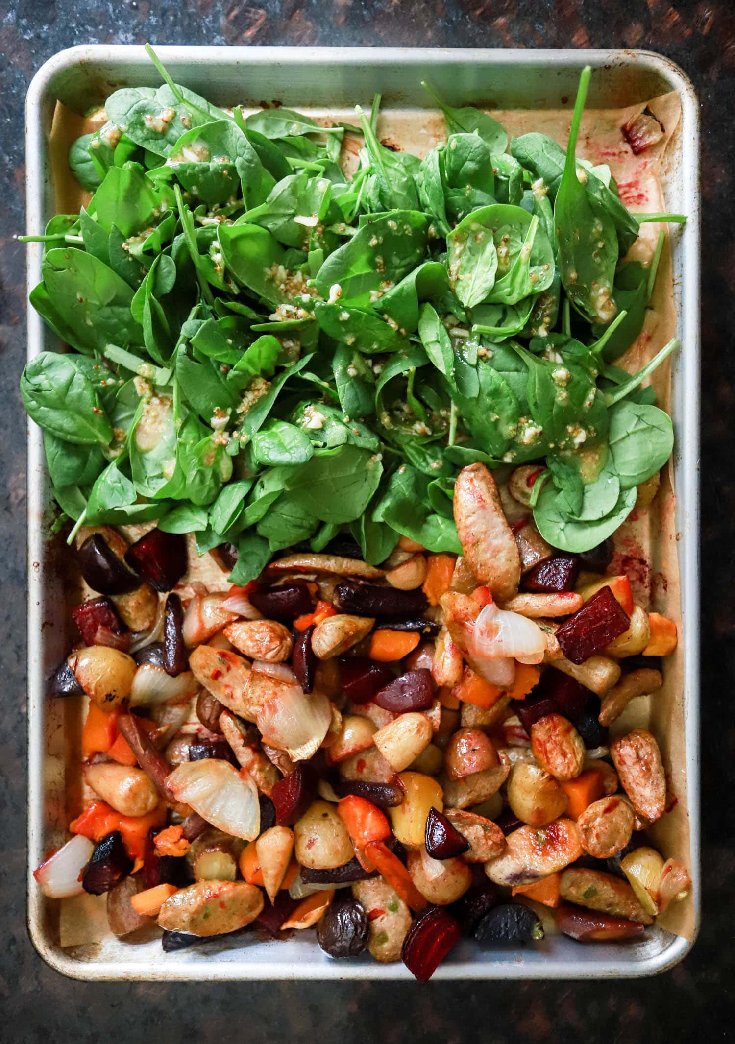 sheet pan sausage recipe with half the pan filled with fresh spinach.