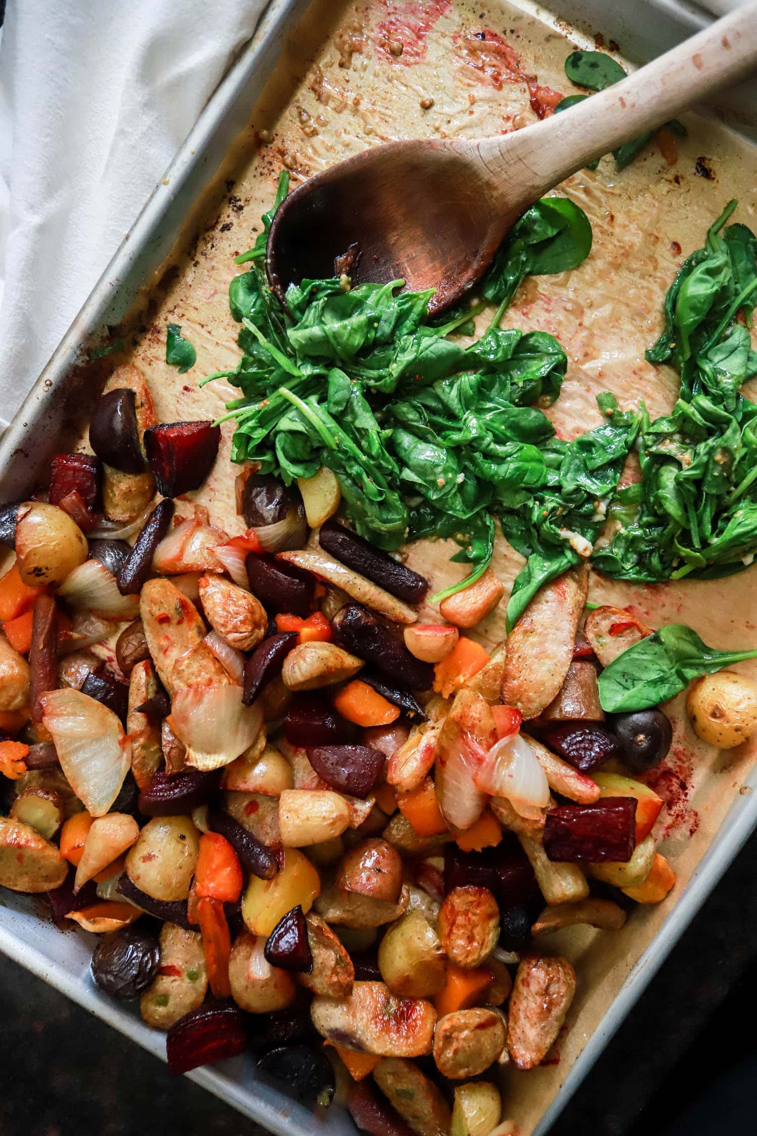 sheet pan chicken sausage and veggies, and wilted spinach with a wooden spoon on a large baking sheet.