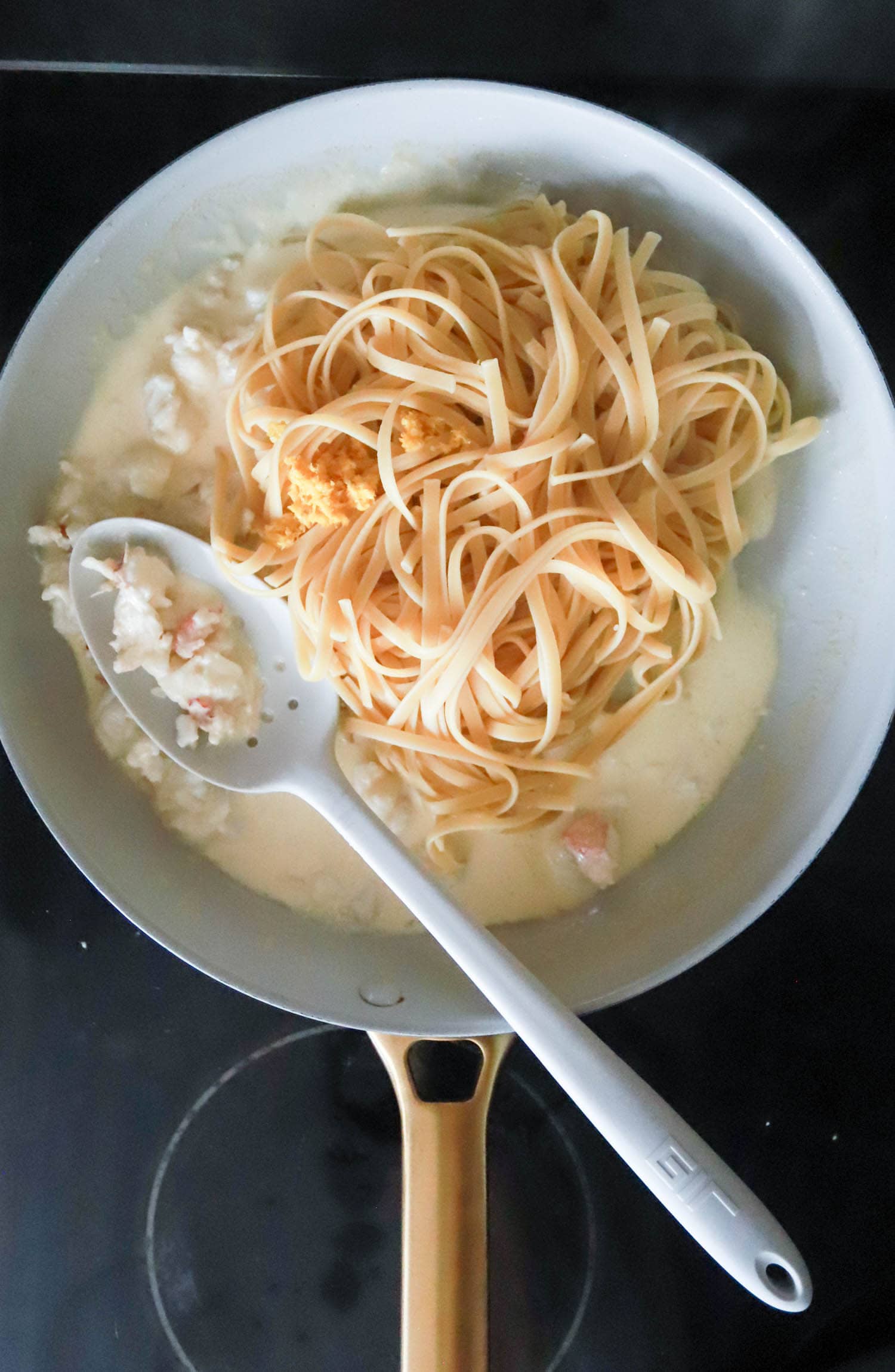 White skillet with lobster pasta cream sauce and white spoon.