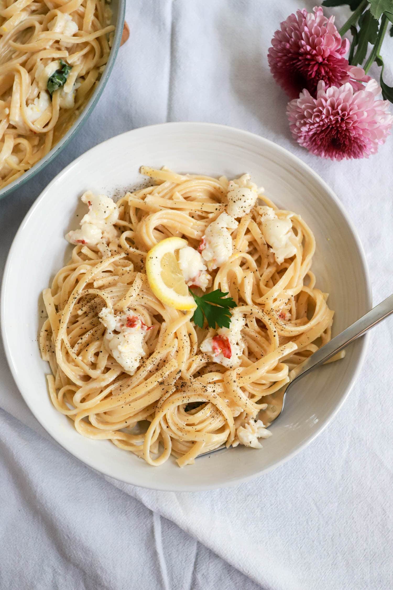 White bowl of lobster with linguine and lemon cream sauce.