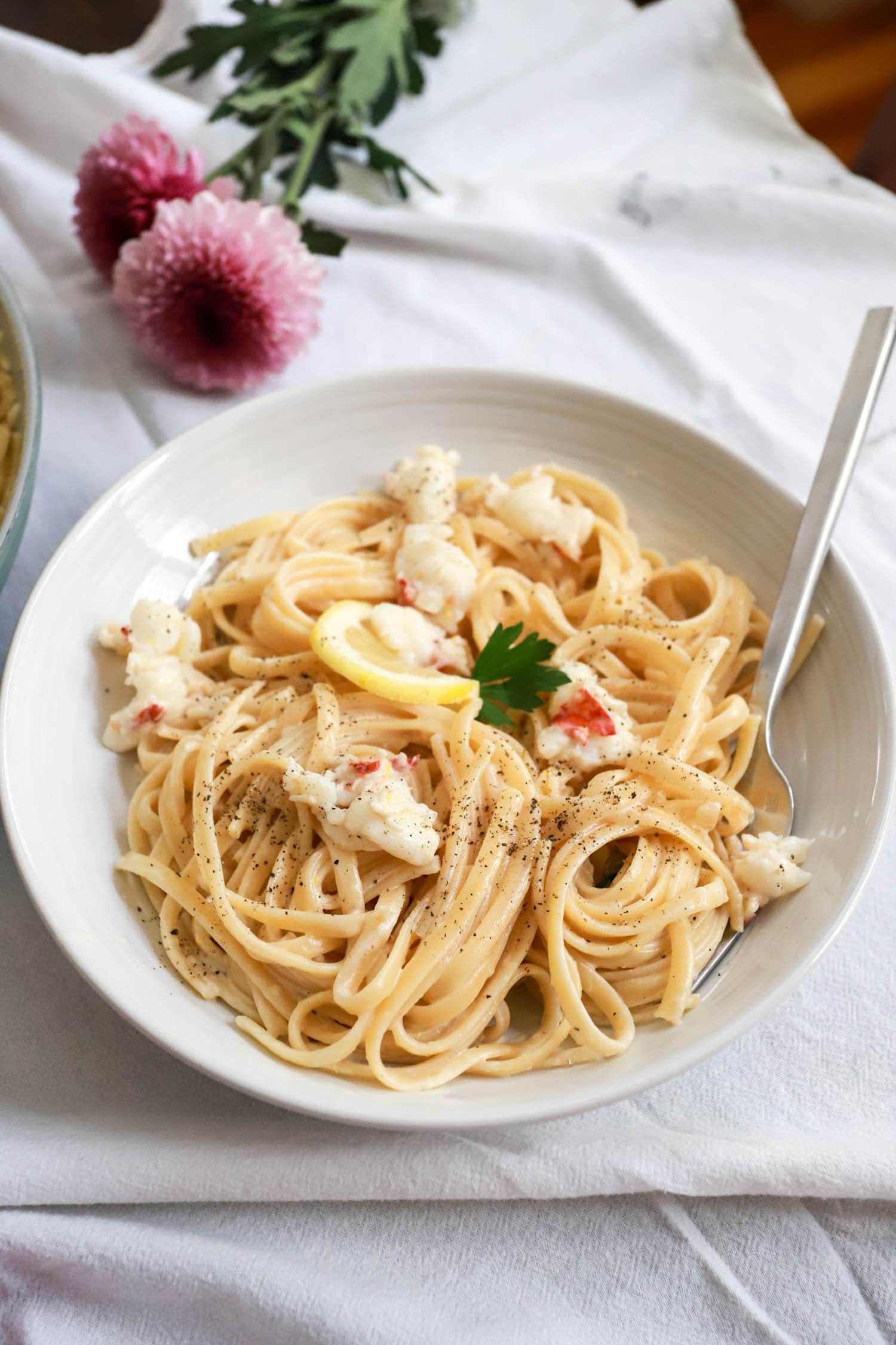 White bowl of lobster tail pasta cream sauce with lemon.
