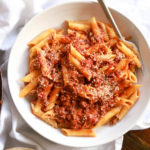 white bowl with penne and meat sauce over a white napkin.